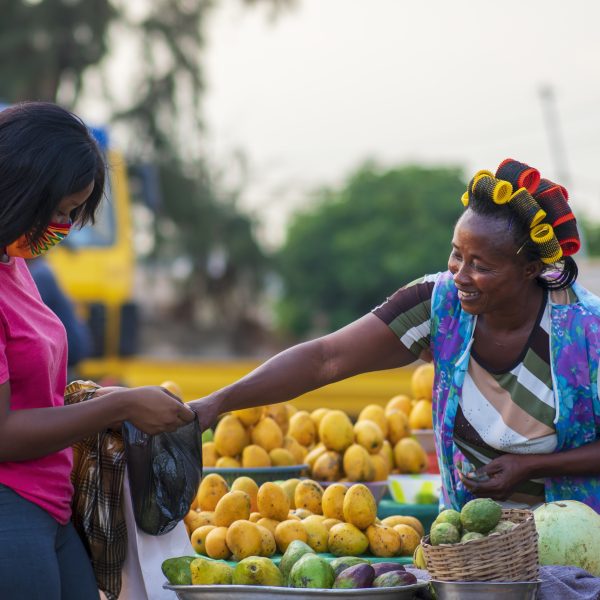 An African American female in a protective face mask shopping for fruit at a market